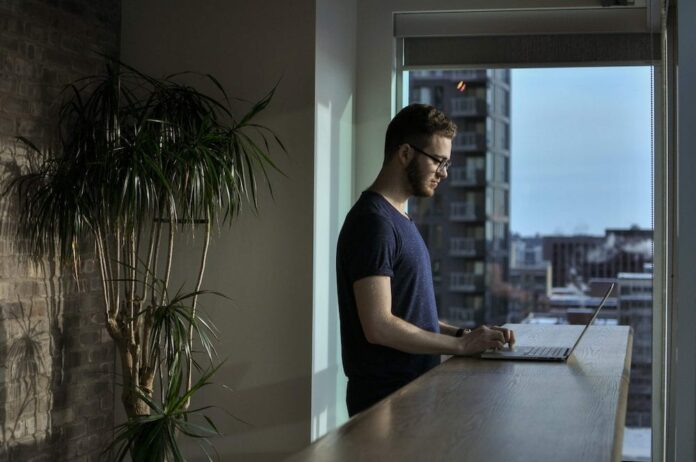 Man standing in an apartment typing on laptop